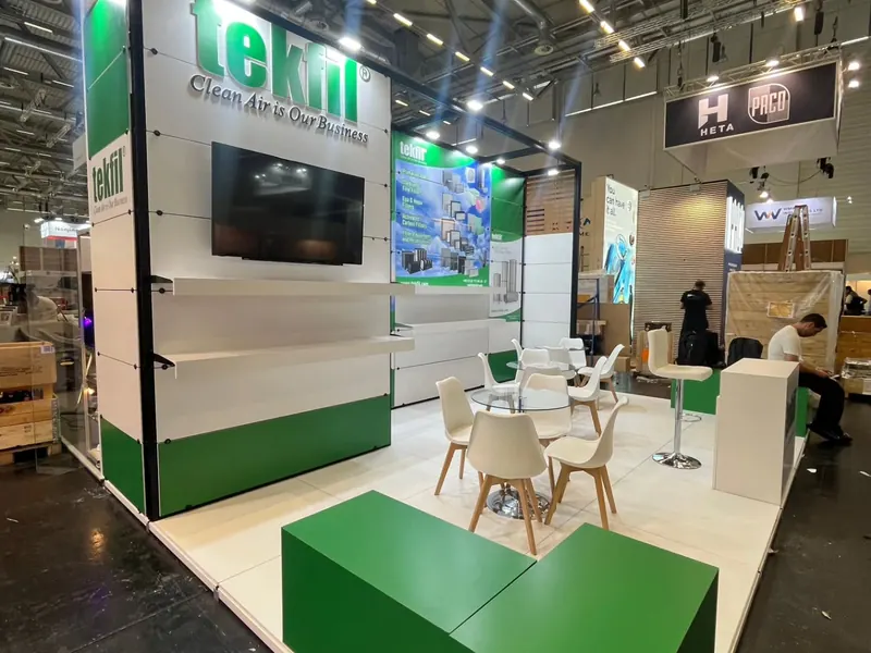 Grün-weißer Messestand mit Bildschirm, weißen Sitzgruppen und grünen Podesten.