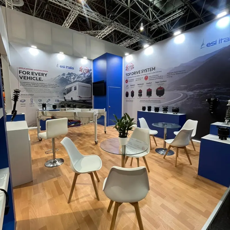 Weiß-blauer Messestand mit Holzboden, Produktauslagen und weißen Stühlen an Glastischen.