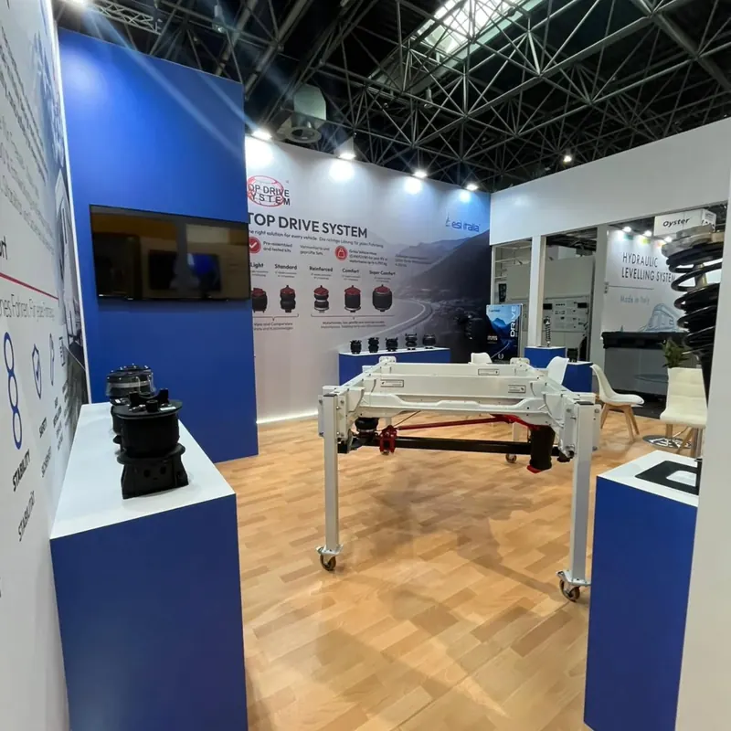 Weiß-blauer Messestand mit Maschinenexponaten, weißen Stühlen und Holzboden.
