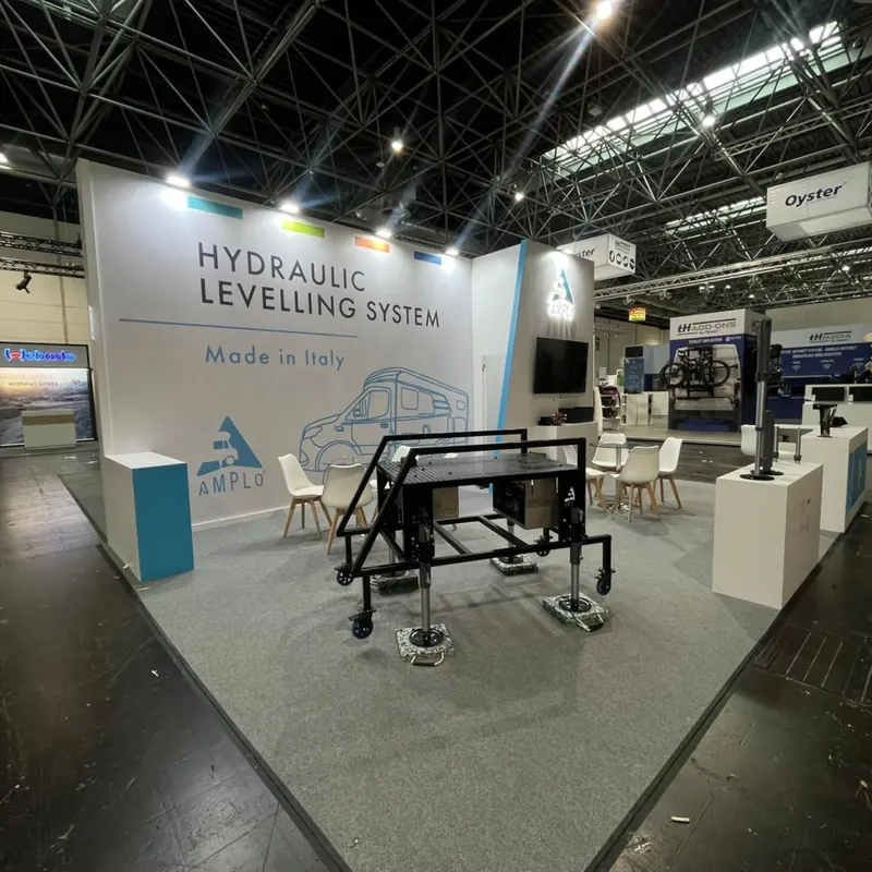 Weißer Messestand mit großer Technikgrafik, Metallgestell und Produktpodesten.