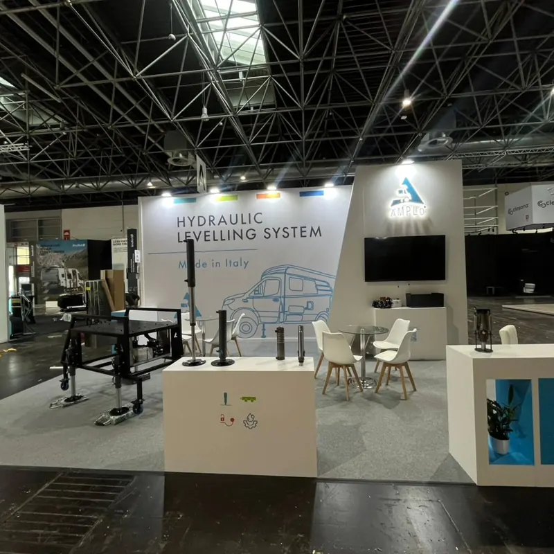 Weißer Messestand mit technischen Exponaten auf Podesten und weißen Sitzgruppen.