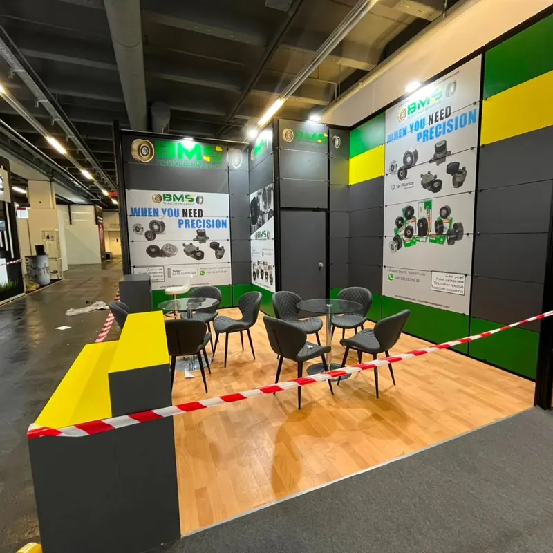 Grün-schwarzer Messestand mit gelbem Stufendisplay und schwarzen Sitzgruppen.