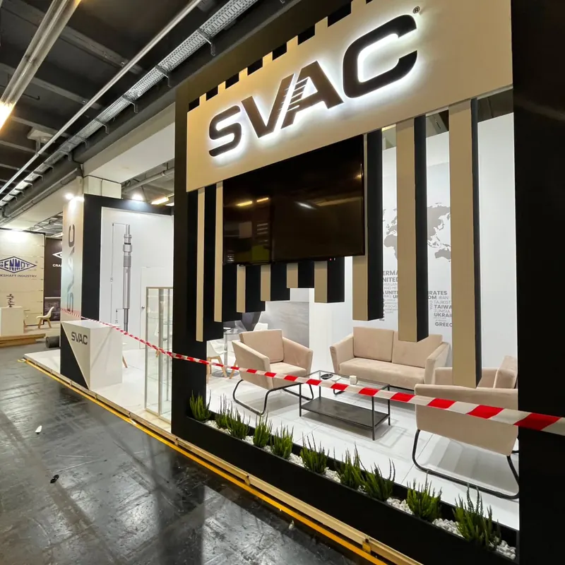 Schwarz-weißer Messestand mit senkrechten Lamellen und heller Lounge hinter Absperrband.