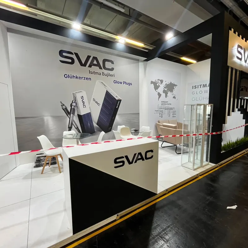 Weiß-schwarzer Messestand mit Empfangstheke, weißen Stühlen und Glasvitrine.
