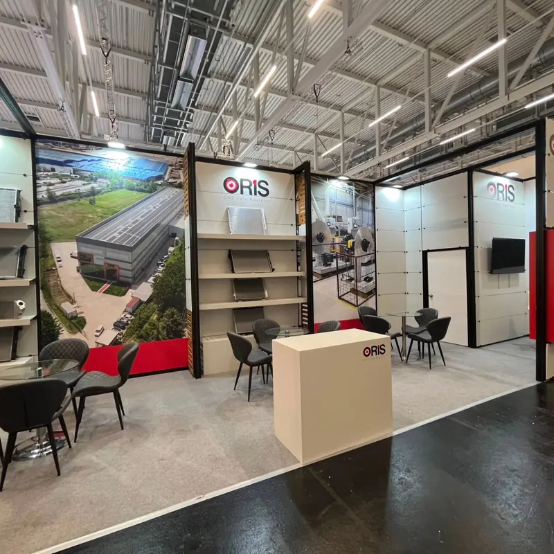 Messestand mit Landschaftsgrafik, offenen Regalen und dunklen Stühlen um kleine Tische.