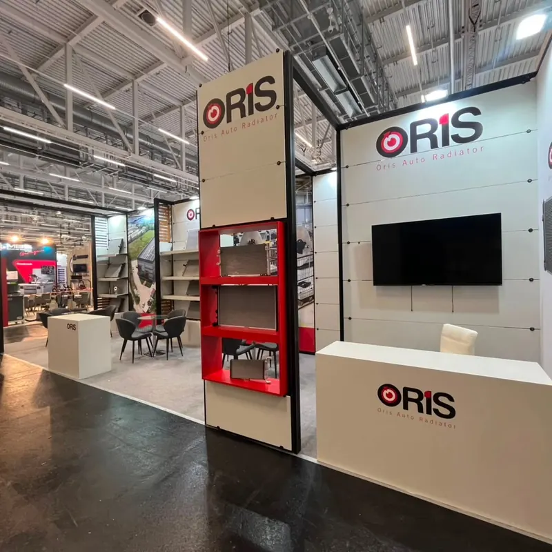 Weißer Messestand mit hoher Holzoptikstütze, roten Regalfächern und breiter Theke.