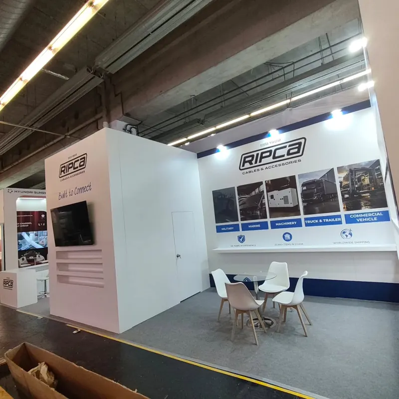 Weißer Messestand mit hellrosa Thekenelement, Bildschirm und blauen Wandgrafiken.