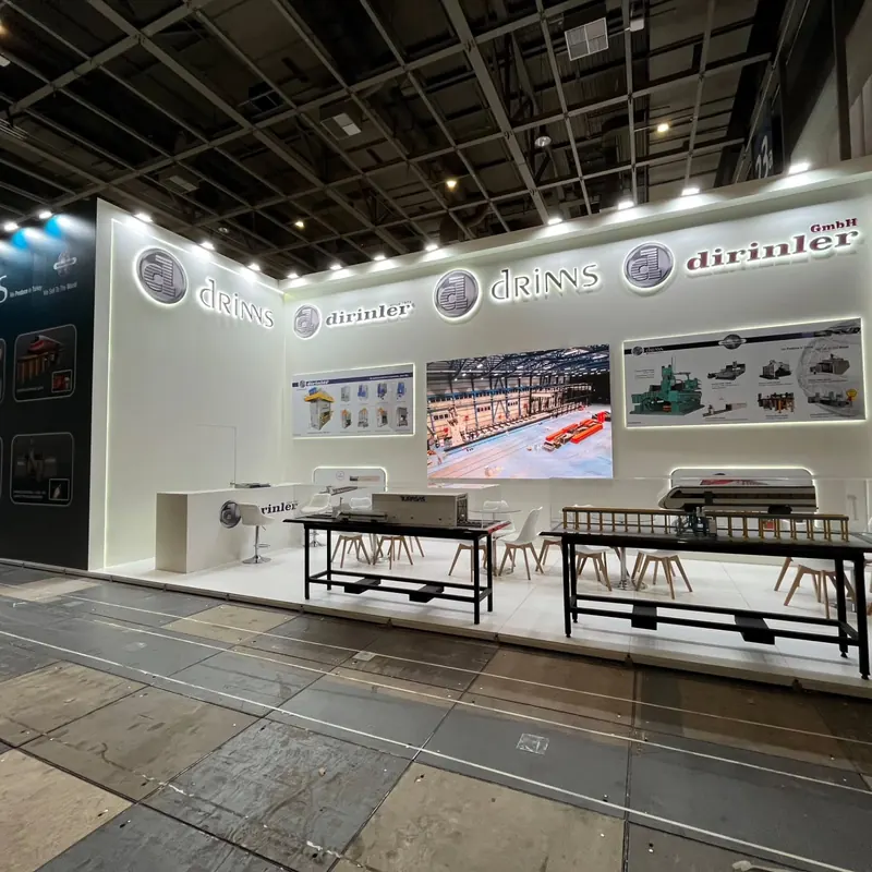 Messestand mit weißer Rückwand, Monitoren, Theke und zwei langen Ausstellungstischen.