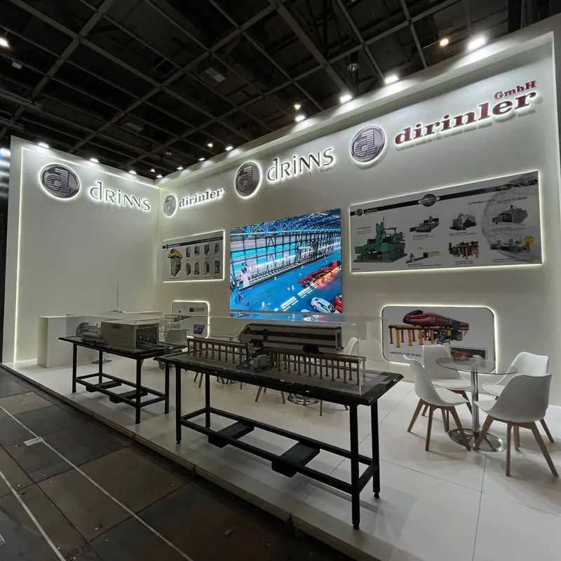 Weißer Messestand mit langen Metalltischen, großen Wandgrafiken und weißen Stühlen.